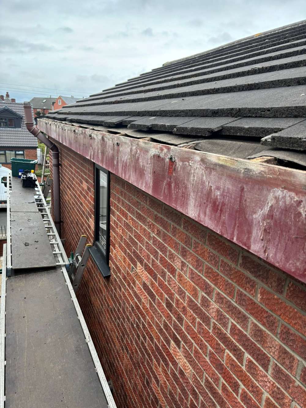 Flaking maroon painted fascia on a red brick house, before