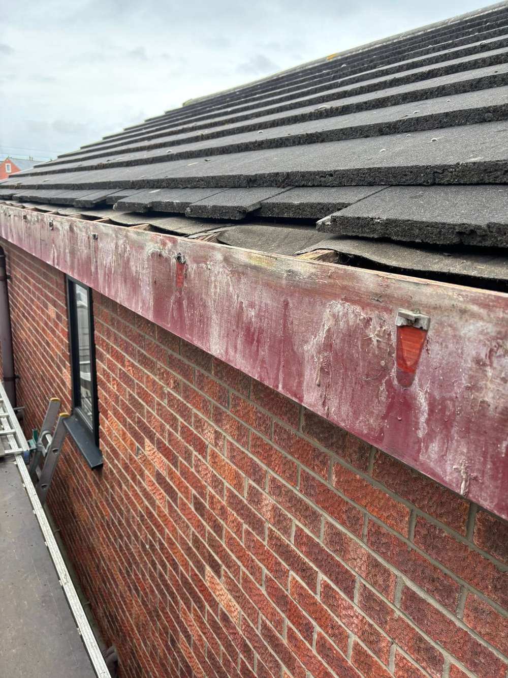 Old painted timber fascia on a red brick house, the paint flaking and the wood split